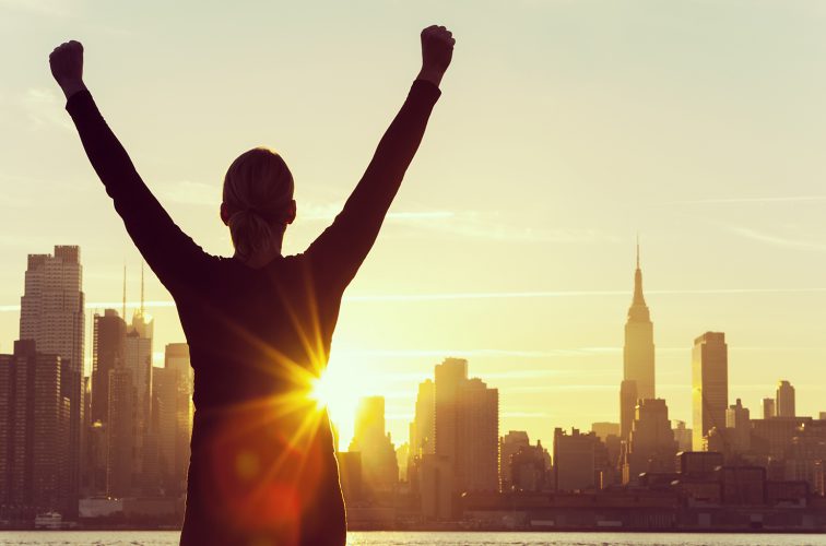 Successful Woman Sunrise New York City Skyline Silhouette of a successful woman or girl arms raised celebrating at sunrise or sunset in front of the New York City Skyline
